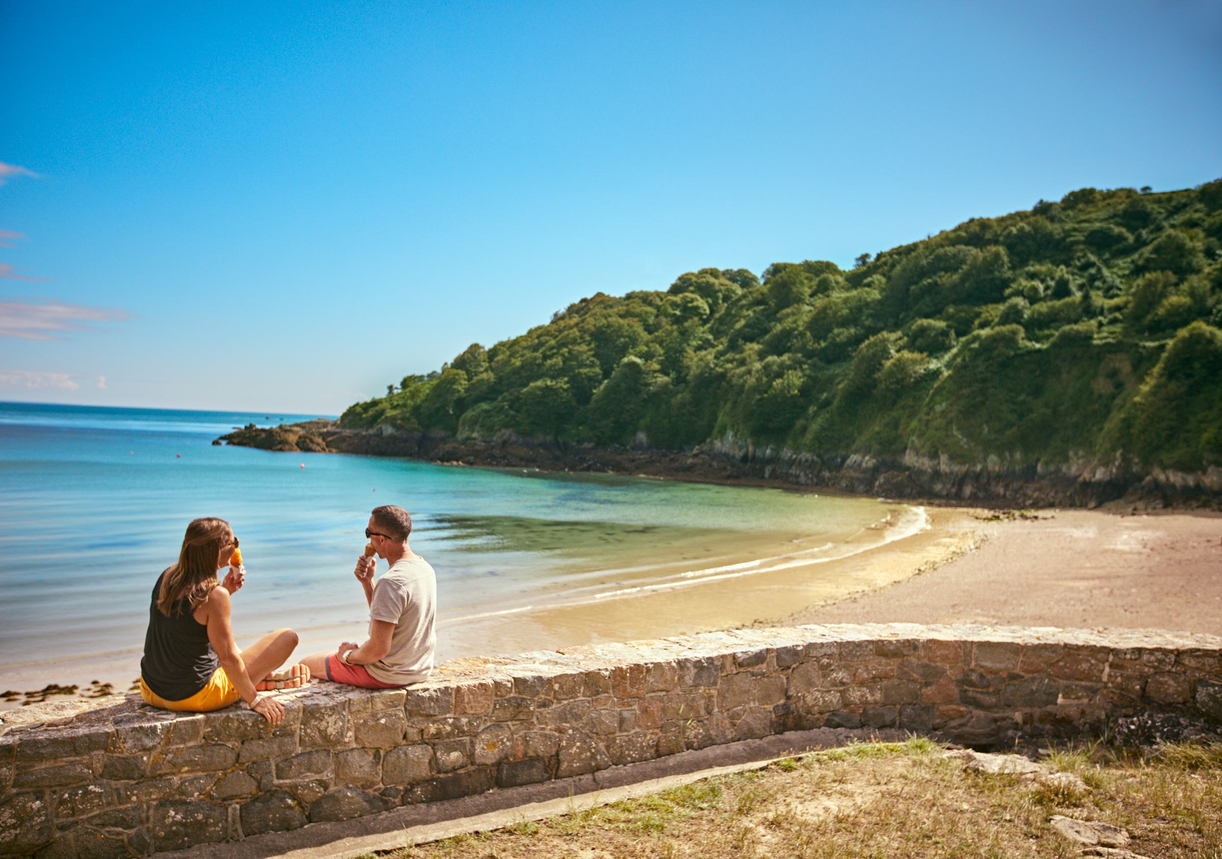 Couple sat on the wall at Fermain Bay eating Ice Creams